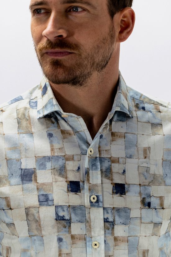 Close-up van het gezicht en de kraag van een man die een overhemd draagt met een mozaïekprint van blauwe, beige en witte vierkanten.