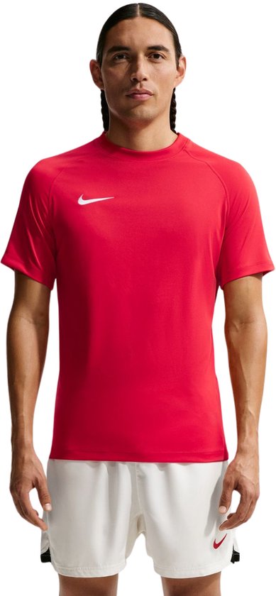 Man met donker haar, draagt een rode Nike Dri-FIT t-shirt en witte sportbroek met zwarte accenten.