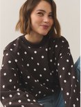 Model met korte bruine bob glimlacht naar links in een donkerbruine sweater met witte polkadotprint.