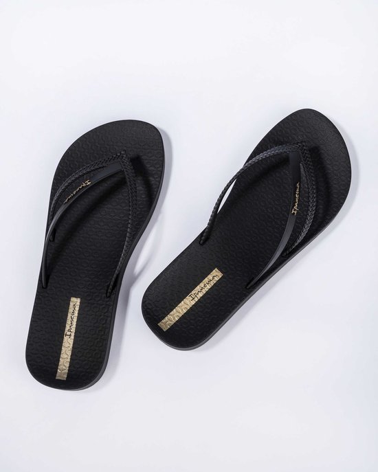 Zwarte Ipanema slippers, schuin van bovenaf gezien, met gevlochten bandjes en gouden logo.