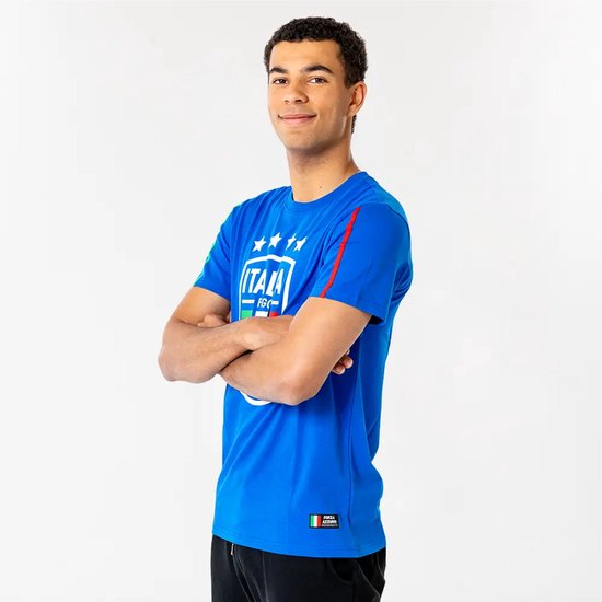Man met armen over elkaar, draagt een blauw t-shirt met Italiaans wapenschild, sterren en mouwstrepen. Zwarte broek.