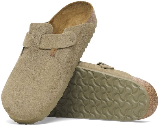 Een beige suède Birkenstock Boston slipper met een verstelbare gesp en een crêpezool. De slipper heeft een opengewerkt detail aan de zijkant.