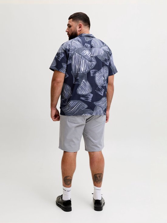 Achterkant model in blauw overhemd met abstracte bladprint en grijze korte broek.