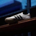 Wit leren Adidas VL Court 3.0 sneaker met bruine zool en zwarte strepen, geplaatst op een houten plank.