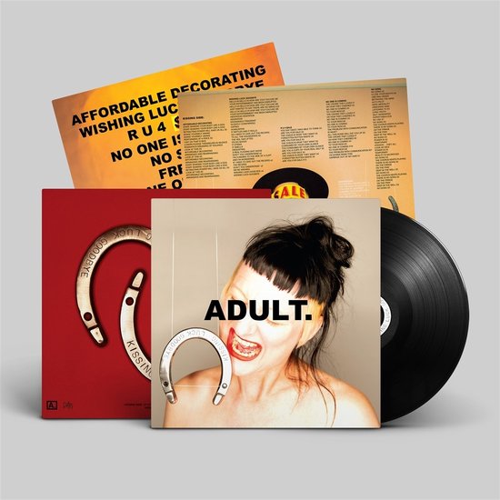 Een vinylplaat en twee hoezen. De voorste hoes heeft een portret van een vrouw met knalroze haar, die een hoefijzer in haar mond heeft. De hoes is rood met gouden tekst.