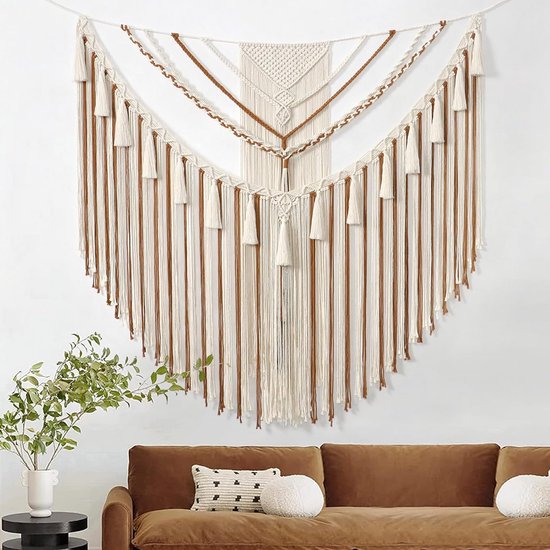 Groot macramé wandkleed in crème en bruin, hangend boven een bruine bank met sierkussens.