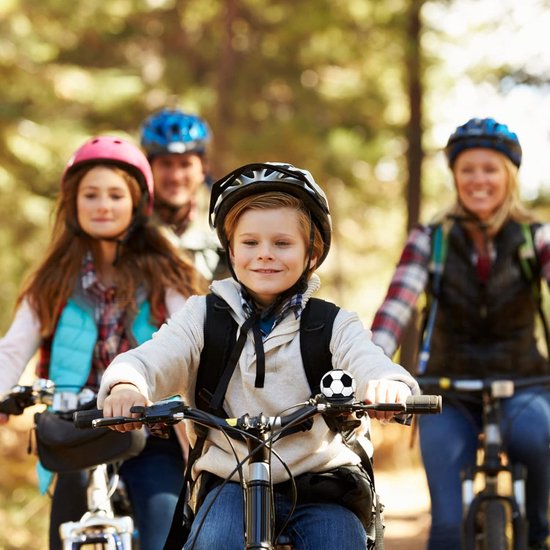 Een gezin van vier personen, inclusief een jongen met een voetbalfietsbel, fietsen in het bos.