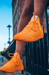 Oranje sneakers met witte veters, gedragen door iemand met een gebogen knie.