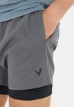 Grijze sportshort met een zwart binnenbroekje. Een zwart 'V'-logo is zichtbaar op de rechterpijp.