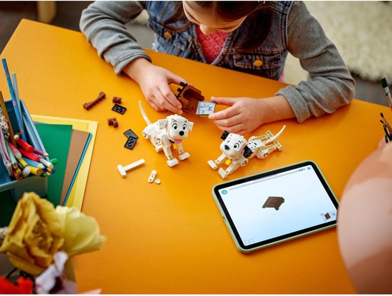 Een meisje bouwt LEGO Dalmatiërs met een tablet, met twee Dalmatiërs en onderdelen.