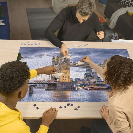 Trois personnes assemblent un puzzle du Tower Bridge au crépuscule.