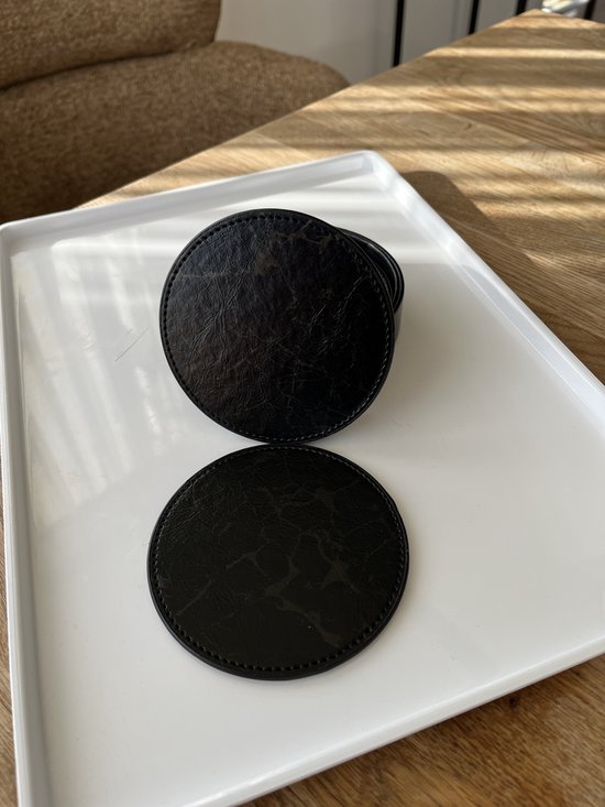 Twee zwarte ronde onderzetters met marmerprint, naast een stapel in een zwarte houder op een witte schaal.