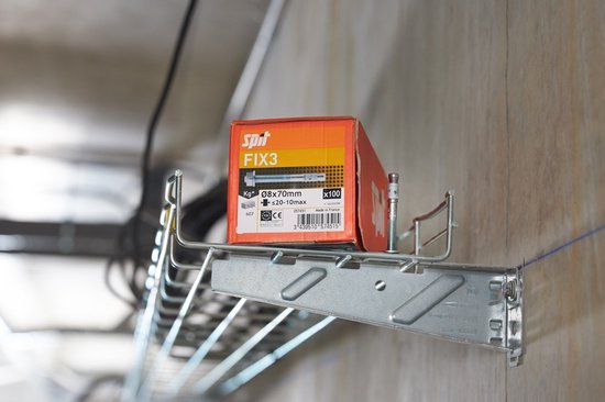 Een rode kartonnen doos met de tekst 'Spit FIX3' bovenop een metalen rail, naast een elektrische kast.