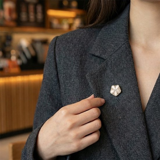 Gouden bloemenbroche met witte parels en diamanten accenten op een donkergrijs jasje.