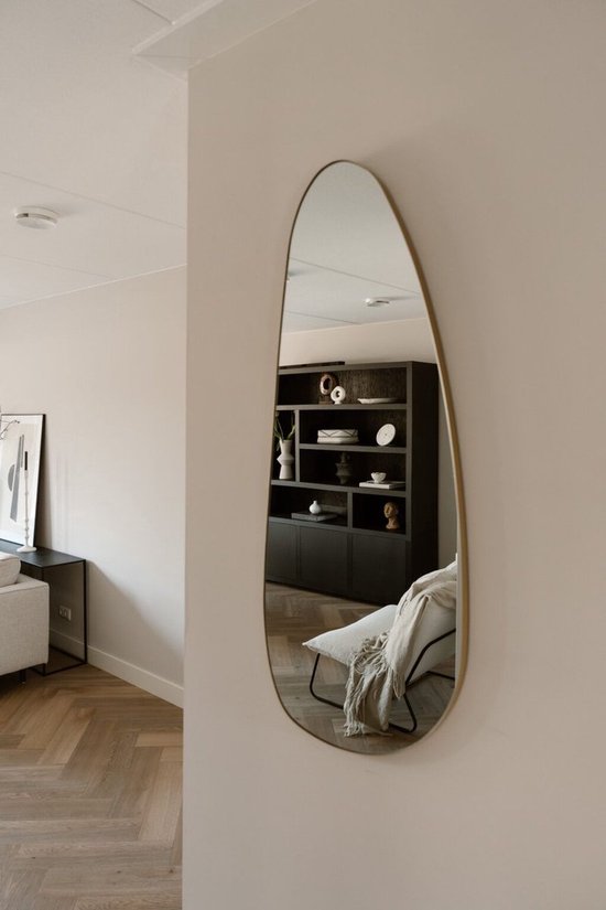 Organische, asymmetrische wandspiegel met gouden rand in een woonkamer