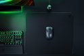 Een zwarte Razer gaming muis op een mat, naast een toetsenbord met groene verlichting.