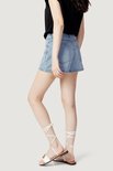 Model met de zijkant naar voren in een lichtblauwe denim skort.