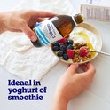 Handen voegen Arctic Blue Omega 3 visolie toe aan yoghurt met bosbessen en frambozen.