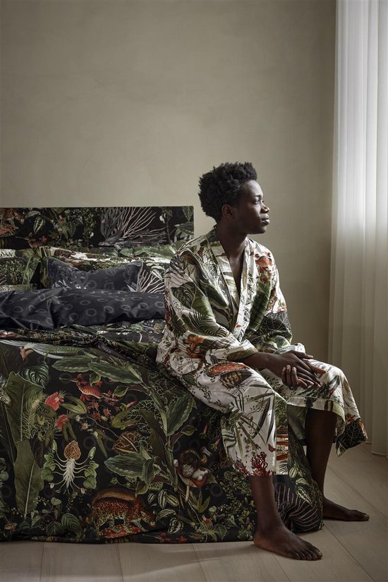 Model zit op een bed, gekleed in een lichte badjas met jungleprint van bladeren en dieren.