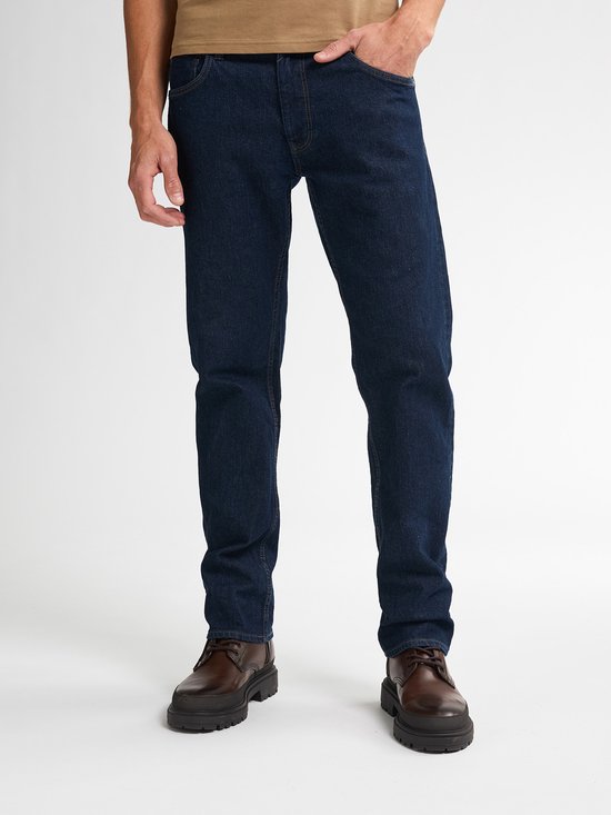 Man in donkerblauwe jeans en bruine schoenen. De broekspijpen zijn recht en de schoenen hebben dikke zolen.
