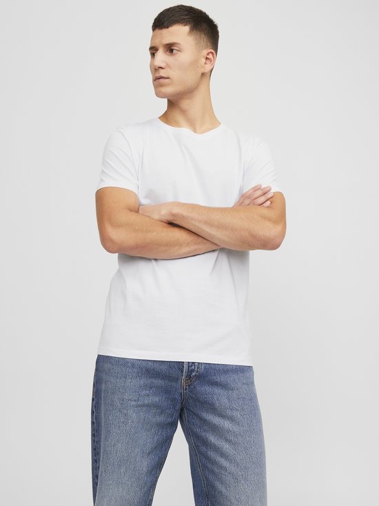 Man met gekruiste armen draagt een wit T-shirt en een spijkerbroek.