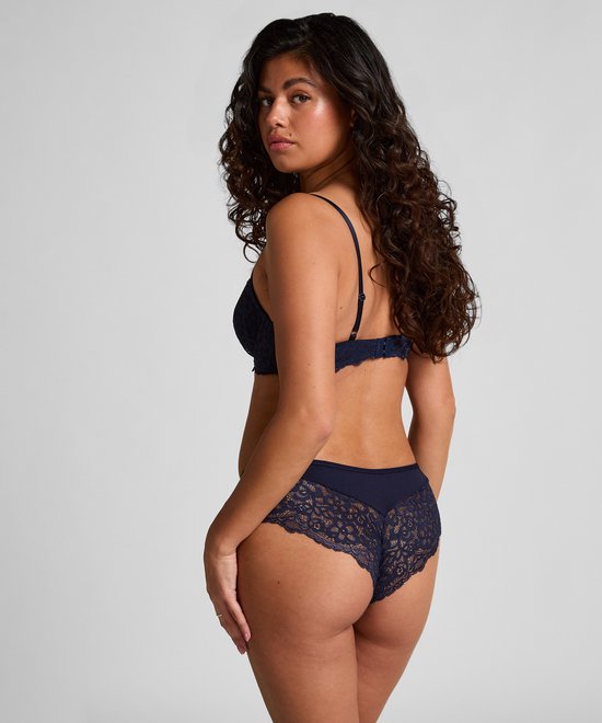 Model met krullend haar draagt een donkerblauwe kanten beugelbeha en bikinislipje, bekeken vanaf de achterkant.