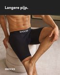 Man zit op een ronde poef en draagt zwarte boxershorts met langere pijpen.