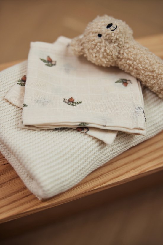 Carré en mousseline crème à imprimé glands, avec une couverture en maille et une peluche beige par-dessus.