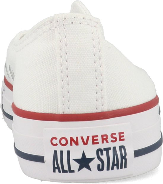 Achterkant van een witte lage Converse sneaker met rode en blauwe strepen en logo.