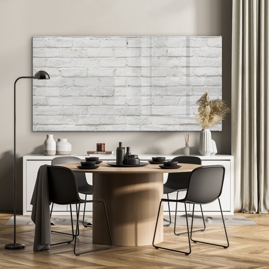 Acrylglas schilderij met witte baksteen textuur, hangend boven een buffetkast in een eetkamer met een ronde tafel en zwarte stoelen.