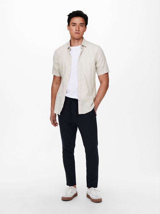 Lichtbeige linnenmix overhemd met korte mouwen, gedragen over wit T-shirt en zwarte broek.