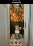Een toiletruimte met opvallende jungle-behang, donkergroene tegels en een gouden wandlamp in de vorm van een aap.