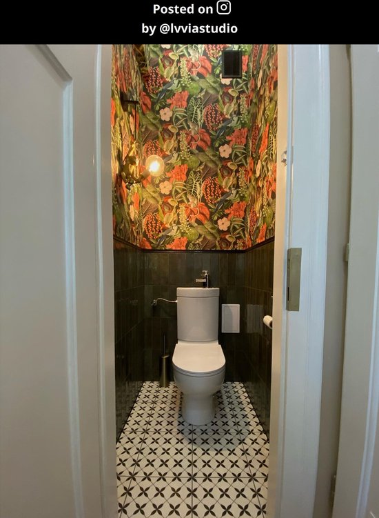 Een toiletruimte met opvallende jungle-behang, donkergroene tegels en een gouden wandlamp in de vorm van een aap.