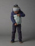 Jongetje met krullend haar, in donkerblauw gebreid vest, donkerblauwe broek, pufferjas met blauw en groen, en grijze muts.