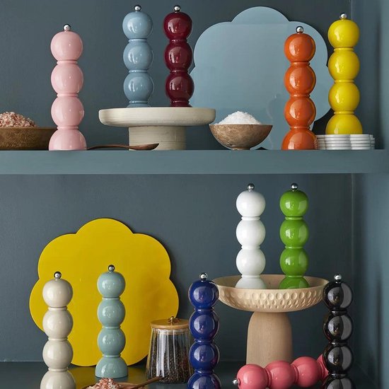 Collectie kleurrijke peper- en zoutmolens in diverse pastel- en felle tinten, tentoongesteld op planken.