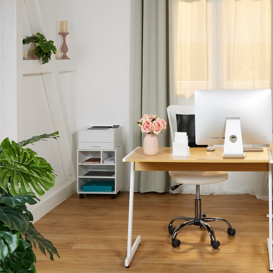 Een bureau met een bureaustoel en een printerkast op wielen, met een computer en een vaas met roze bloemen.