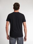 Man met zwarte T-shirt met korte mouwen en een kleine witte 'Petrol' tekst opdruk op de linkerborst, gezien vanaf de achterkant.