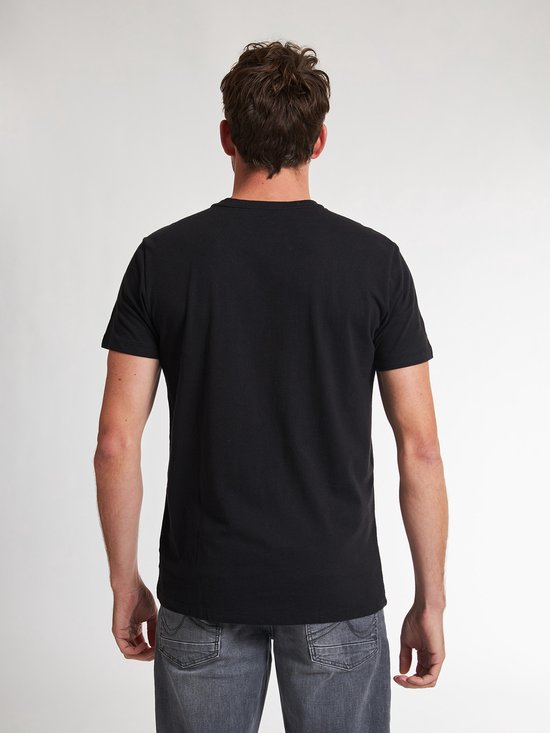 Man met zwarte T-shirt met korte mouwen en een kleine witte 'Petrol' tekst opdruk op de linkerborst, gezien vanaf de achterkant.