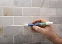 Hand met witte voegpen die voegen van marmerlook tegels vernieuwt.