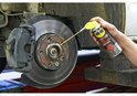 Man spuit WD-40 Specialist Super Kruipolie op een remklauw van een auto.