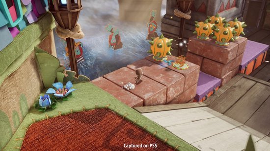 Sackboy rent op een oranje bakstenen pad met pompoenvijanden, terwijl water en vreemde planten te zien zijn.