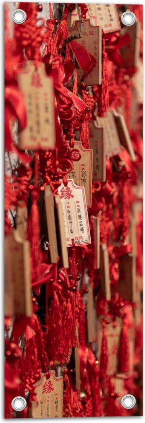 Tuinposter – Rode Sleutelhangers met Chinese Tekens aan een Muur - 20x60 cm Foto op Tuinposter (wanddecoratie voor buiten en binnen)
