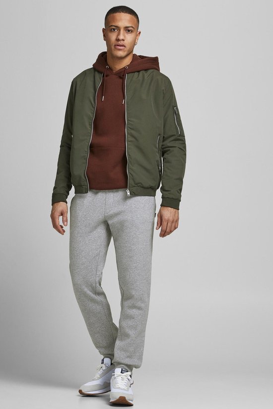 Man in een lichtgrijze joggingbroek, groene bomberjack en bruine hoodie.