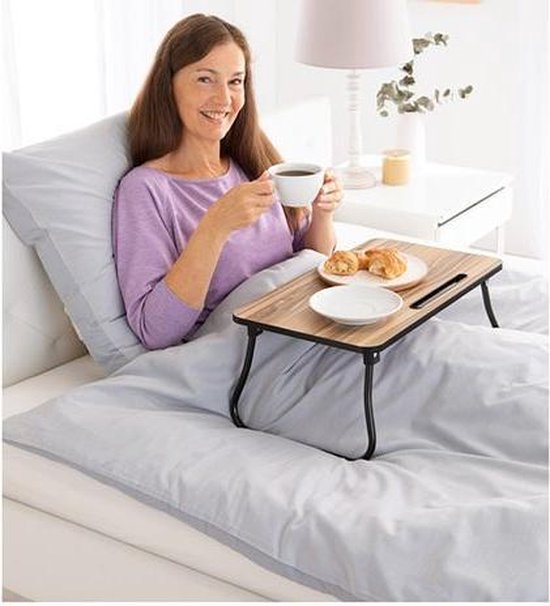 Vrouw in bed met houten bedtafel en ontbijt.