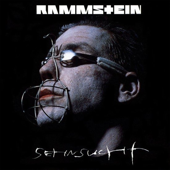 Albumcover van Rammstein's Sehnsucht met een man met een metalen mondbeugel en een lepel in zijn oog.