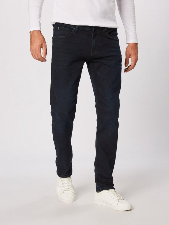 Man in een donkerblauwe jeans en een wit shirt met lange mouwen.