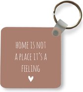 Sleutelhanger - Uitdeelcadeautjes - Engelse quote Home is not a place it's a feeling met een hartje tegen een bruine achtergrond - Plastic