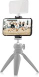 Een smartphone met een foto van vijf springende meisjes op een festival, bovenop een MOJOGEAR LED lamp en een grijs statief.