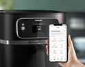Hand houdt smartphone met Airfryer recepten app voor de zwarte Philips Airfryer Combi XXL.