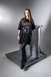 Vrouw met lang blond haar draagt een zwart oversized T-shirt met schedel- en rozenprint, leren legging en zwarte laarzen.